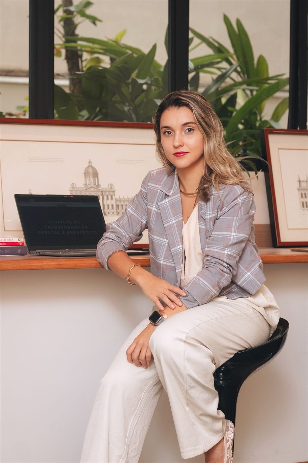 Nathalia Mancini de blazer, sentada em seu espaço de trabalho